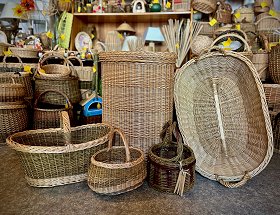 Einkaufskörbe, Wäschebehälter, Klammer- und Wäschekörbe in verschiedenen Formen, Farben und Größen sind hier zu sehen. Sie stehen auf dem Fußboden im Geschäft vor zahlreichen anderen Flechtwaren.