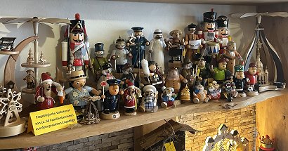 Erzgebirgische Räuchermänner, Pyramiden und Nussknacker sind in einer großen Zahl auf einem Wandregal zu sehen. Die Figuren sind sehr bunt gestaltet. Je eine kleine, etwa 25 cm hohe Pyramiden am rechten und linken Bildrand sind naturbelassen mit der Seiffener Kirche oder mit kleinen geschnitzten Figuren.