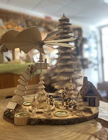 Auf dem gesamten Bild dominiert eine geschnitzte Pyramide aus hellem Holz mit Räucherhaus, Futtergrippe und Vogelhaus. Ein geschnitzter Baum steht mittig auf dem Drehteller und dient der Befestigung der Pyramidenflügel. Kleine Waldtiere und Holzfiguren runden das Bild ab.