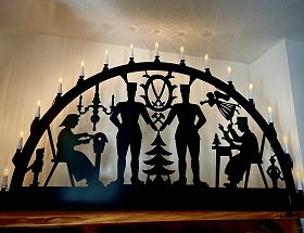 Das gesamte Bild wird von einem schwarzen Aussenlichterbogen aus Metall eingenommen, der auf einem Wandregal steht. Er ist von fünfzehn elektrischen Kerzen beleuchtet und zeigt als Motiv zwei Bergmänner, Schnitzer und Klöppelfrau. Er kann in Breiten von 1,00 m und 1,50 m erworben werden.