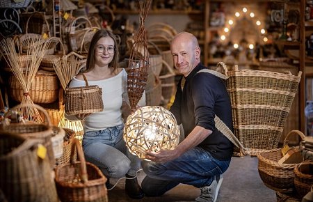 Geschäftsinhaber Mirko Trinks hockt mit seiner Tochter Sarah inmitten von geflochtenen Körben und hält eine beleuchtete Weidenkugel in der Hand.